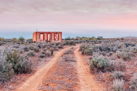 Dawn skies over an abandoned and run down building among the salt bush and red soils in outback Australia