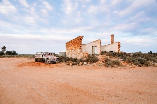 The remains of an old stone home slowly crumbling away, beside it sits a vintage car slowly rusting under the harsh Australian sun on the inland desert of Australia. Remnants of a bygone era