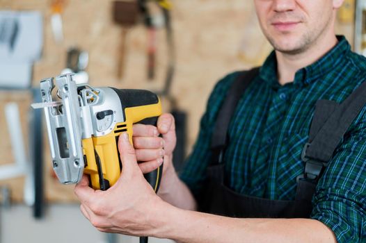 Portrait of a man with an electric jigsaw on wood in the workshop