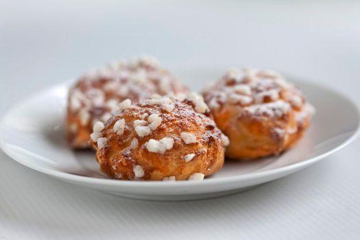 Small cream puffs on a white plate with pieces of sugar