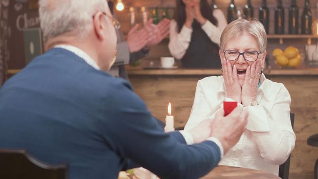 Senior man giving diamond engagement ring in little red box to his woman. Couple love. Romantic couple.