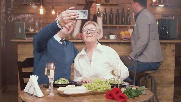 Romantic old couple taking a selfie during while they are having lunch in a restaurant. Man and woman in their sixtie. Senior couple.