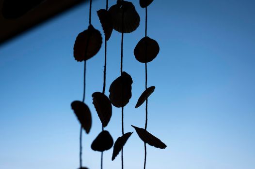 Silhouette of a dream catcher made with seashells against blue sky.