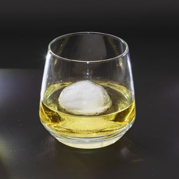 Whiskey on the rocks in a round drinking glass as studio shot with a black background