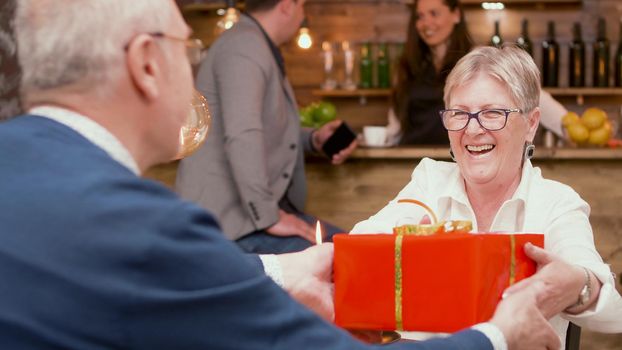 Happy senior woman when she's receiving a red gift box from her husband during their date. Cheerful senior couple. Couple smiling.