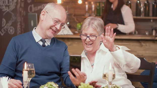 Senior couple having a video call during mealtime in a restaurant. Senior couple smiling. Romantic old couple. Couple in their sixties.