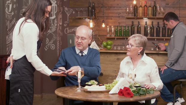 Senior man paying dinner at the end of the date with a lovely old lady. Romantic couple. Man and woman in their sixties.