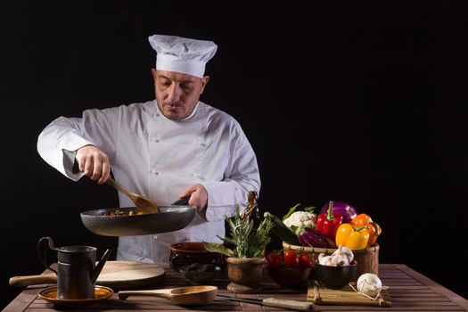 Chef in white uniform and hat with ladle mixes the ingredients onto the cooking pan before serving while working in a restaurant kitchen