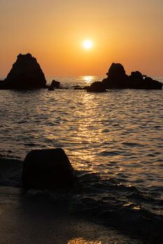 A beautiful view of orange sunset with rocks in Calabria, Mediterranean Sea, Italy. Tropical colorful sunrise landscape. Seascape