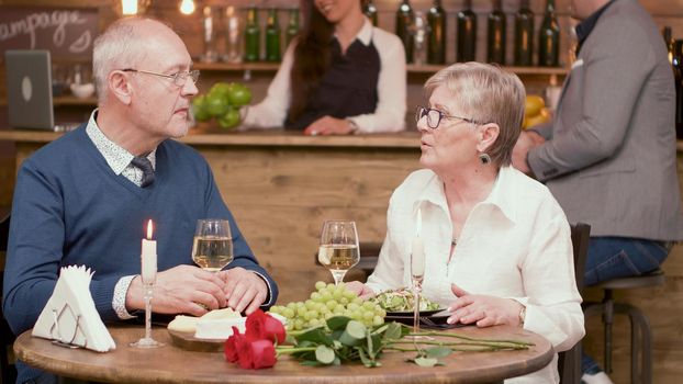 Old couple sitting at the table in a restaurant and drinking wine. Telling her stories. Relaxed couple. Cheerful couple. Romantic couple.