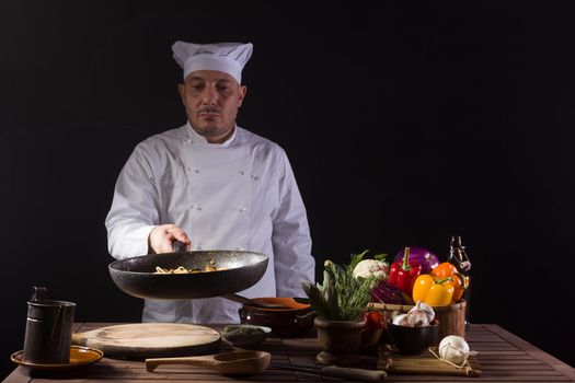 Chef in white uniform and hat with looking the cooking pan before serving while working in a restaurant kitchen