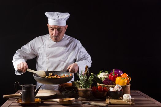 Chef in white uniform and hat with ladle mixes the ingredients onto the cooking pan before serving while working in a restaurant kitchen