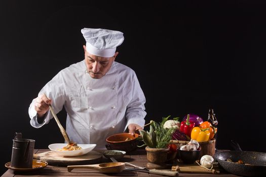 Male chef in white uniform prepares spaghetti with vegetables on the dish before serving while working in a restaurant kitchen