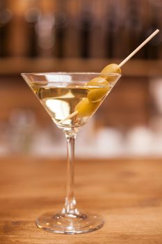 Delicious martini drink with green olives on stick over a wooden bar counter. Fresh drink. Celebration drink.