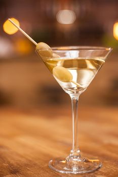 Closeup of a martini glass with olives on a wooden table in a resturant. Fresh drink. Tasty drink. Alcoholic drink.