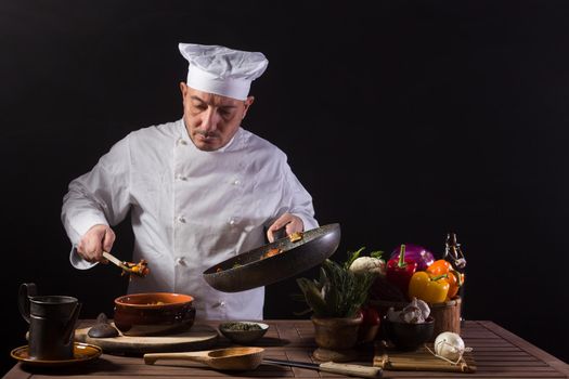 Male chef in white uniform preparing food plate with vegetables before serving while working in a restaurant kitchen