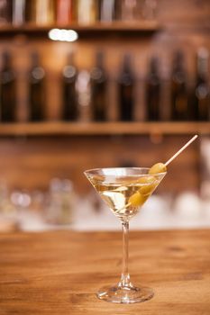 Glass of dry martini with green olives on a rustic wooden bar counter. Refreshment drink. Nightlife. Closeup