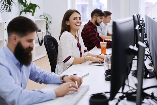 People working in modern IT office. Group of young programmers and software developers sitting at desks working on computers. Team at work.