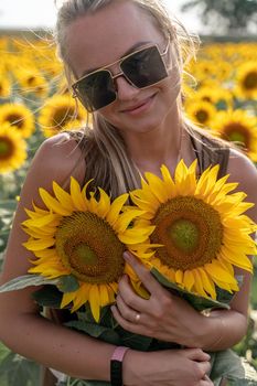 Beautiful woman in sunflower field at sunset enjoying summer nature. Attractive blonde with long healthy hair