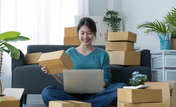 Startup happy Asian woman business owner works with a box at home, prepare parcel delivery SME supply chain, procurement, package box to deliver to customers, Online SME business entrepreneurs ideas,.