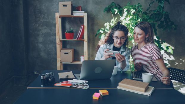 Young enterpreneurs are talking and looking at smart phone while sitting at desk in modern office.