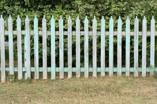 a small blue wooden fence stands against the background of a high red metal fence.