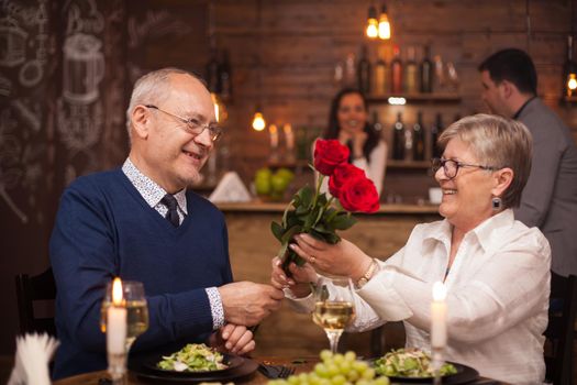 Cheerful senior couple happy about their date. Husband giving flower to his wife. Enjoying retirement.