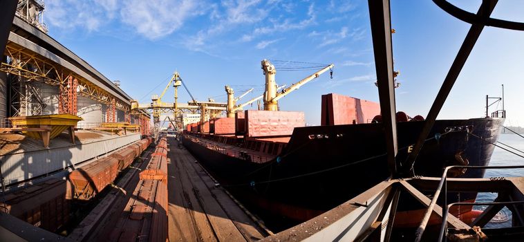 Loading grain into holds of sea cargo vessel in seaport from silos of grain storage. Bunkering of dry cargo ship with grain.