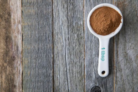 Ground cinnamon in a porcelain tablespoon on a wooden surface with copy space.