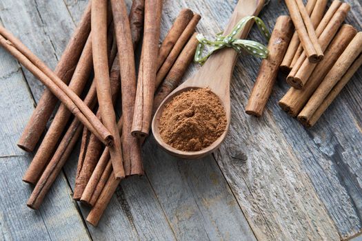 Wooden spoon filled with ground cinnamon and surrounded by cinnamon sticks.