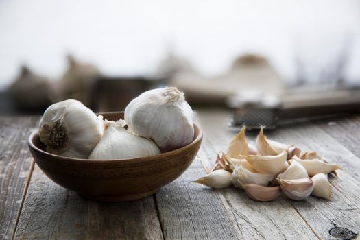 Garlic heads in bowl and cloves on wooden table