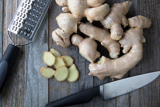 Ginger root and slices with knife and shredder on cutting board.