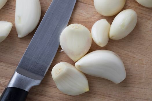 Close up of peeled garlic cloves and knife viewed from directly above.