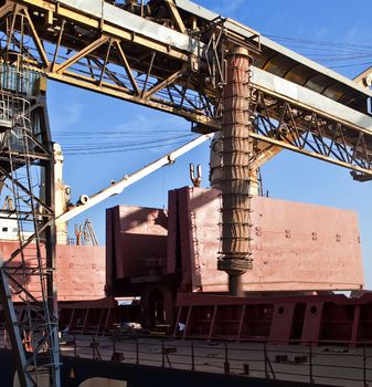 Loading grain into holds of sea cargo vessel in seaport from silos of grain storage. Bunkering of dry cargo ship with grain.