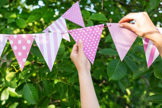 Triangular flags of a beautiful pink color, against the backdrop of a green garden. Festive decor - the concept of celebrating a birthday, anniversary, holiday