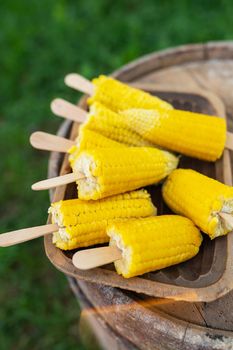 Boiled sweet corn with salt and butter on a stick on a wooden plate. Summer vegan dinner or snack, preparing for the grill. Vertical photo