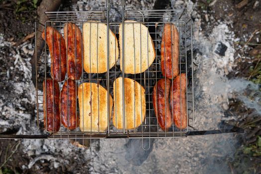 Grilled pork sausage on a cast-iron grill along with bread, top view. Barbecue, outdoor recreation