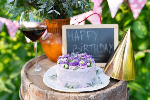 A very beautiful bento cake with purple, veri peri, matthiola flowers on a background of pink flags. Birthday. In the background, a bouquet of flowers, a jug of flowers, a cap for the head, a board with an inscription