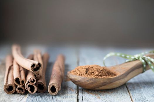 Cinnamon sticks and power in wooden spoon on wooden surface, close up with copy space.