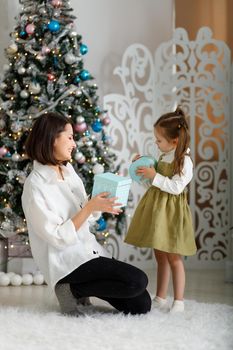 Cute little girl with her mother give each other new year gifts in christmas interior. Vertical, copy space.