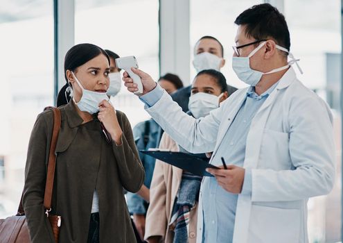 Travel medical healthcare worker testing covid temperature at airport using infrared thermometer. Professional doctor doing a coronavirus check up on a woman at an office entrance.