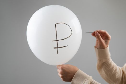 Caucasian woman pops a balloon with a ruble inscription with a needle