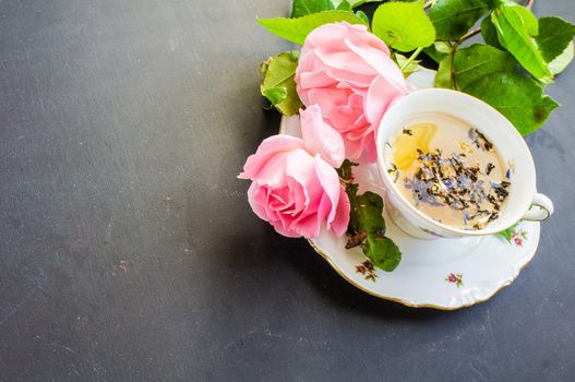 Cup of floral tea in vintage cup and pink roses on wooden table with copyspace