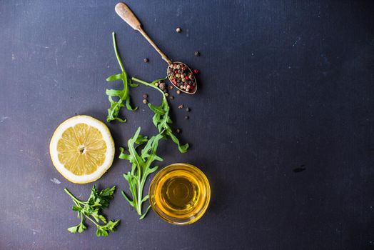 Flat lay of organic ingredients for salar - rukkola, pepper grain and lemon with oil on blackboard