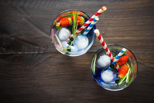 Detox summer drink with rosemary, strawberry, and bilberry with bright color straws on dark wooden table