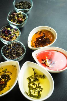 Different types of tea, green tea, peony and ginger tea, rose bud and wild flowers tea on dark wooden background with copyspace