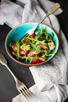 Spring healthy salald with fresh organic tomatoes, radish and rukkola herb on rustic plate with napkin and silverware