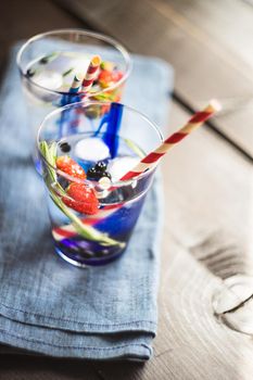 Detox summer drink with rosemary, strawberry, and bilberry with bright color straws on dark wooden table