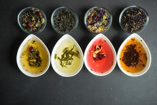 Different types of tea, green tea, peony and ginger tea, rose bud and wild flowers tea on dark wooden background with copyspace