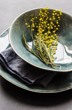Festive table setting for Easter dinner with bright easter eggs and mimosa flowers on rustic plate